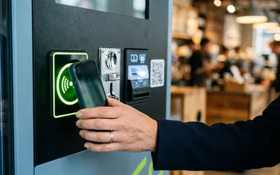 Pago con el móvil en el lector contactless de una máquina expendedora, junto al monedero, el lector de billetes y un código QR